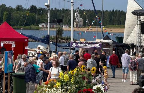 Markkinat käynnissä Raahen Rantatorilla. Kävijöitä, kukkaistutuksia ja taustalla meri.