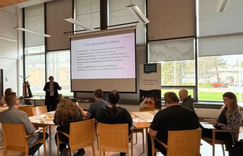 Työpajan osallistujia seuraamassa koulutusta pöytäryhmissään.