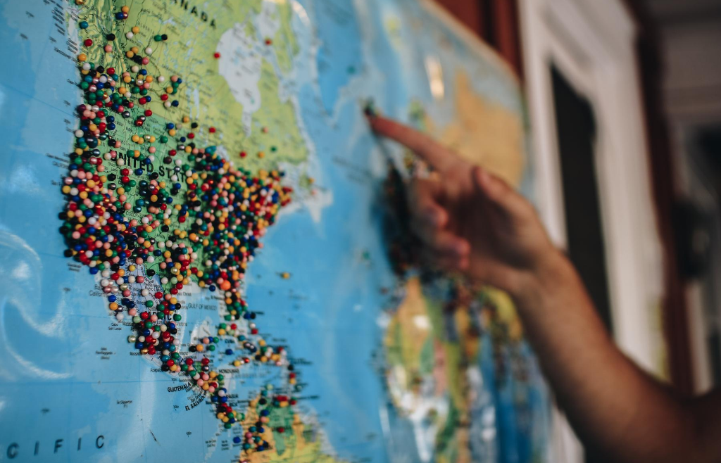 Maailman kartta seinällä, jossa värikkäitä nuppineuloja.